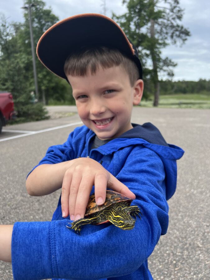 A boy holding a turtle and smiling.